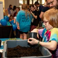 Father and young child plant seed at a table at student project showcase